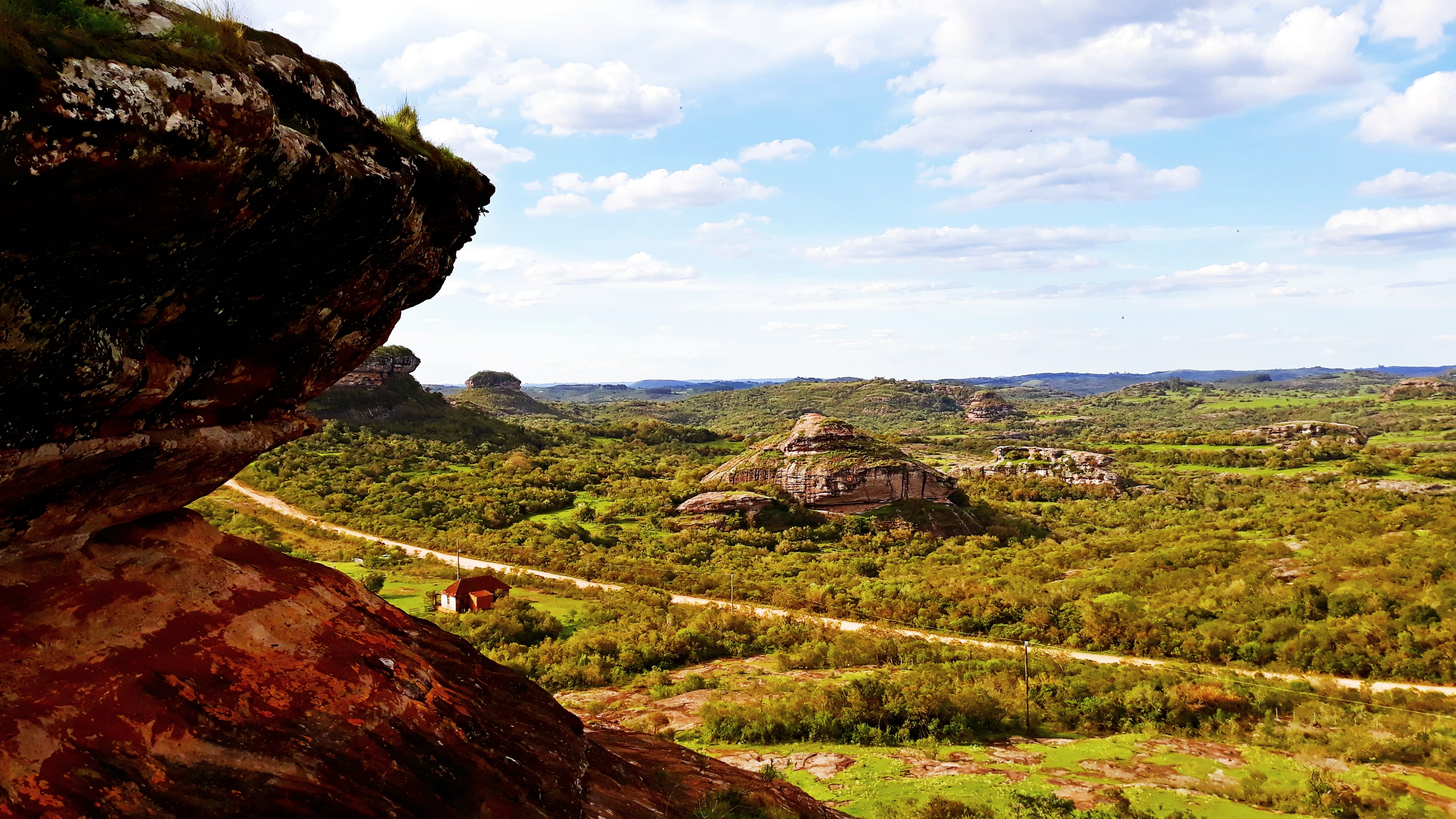 Geoparque de Caçapava do Sul deve receber visita de certificação da Unesco em agosto - Divulgação Foto colorida do Geoparque de Caçapava do Sul com rocha à esquerda e paisagem com campos formações rochosas ao fundo