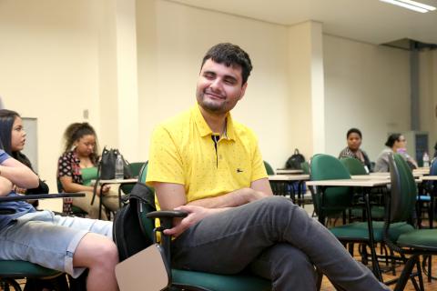 O estudante Lúcio Lopes apresentou trabalho sobre acessibilidade nos restaurantes universitários no 10º Siepe (Foto: Milene Marchezan) Jovem homem sentado, braços cruzados no colo, cabelo castanho, curto, olhos fechados. Camisa polo amarela, calça jeans.