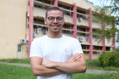 Danilo Xavier veio da Bahia para cursar jornalismo em São Borja Danilo Xavier, um menino branco, de óculos e camiseta branca, com os braços cruzados, parado em frente a um prédio