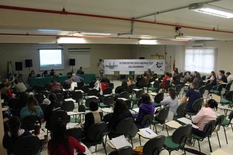 Propostas foram apresentadas durante assembleia Pessoas sentadas em cadeiras olham para a exposição que é feita por meio de projeção de imagem sobre tela branca. à direita da tela com projeção está uma faixa promocional do evento